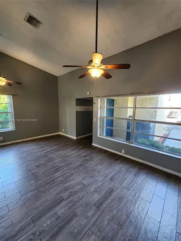 an empty room with wooden floor chandelier fan and windows