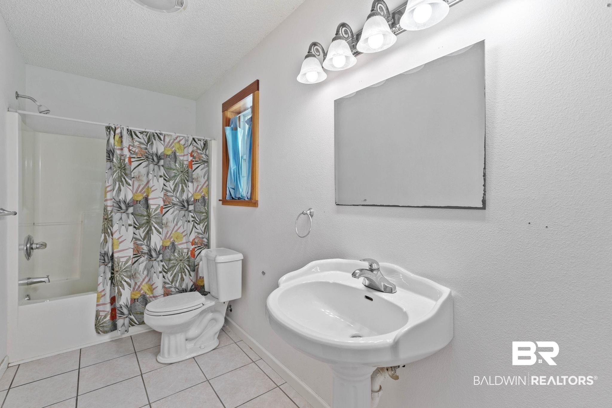 20219 Greek Cemetery Road Robertsdale, AL 36567 - Photo 28 of 41 Full bathroom featuring a pedestal sink with chrome faucet, a rectangular mirror under a four-light vanity fixture, a toilet, and a bathtub with shower