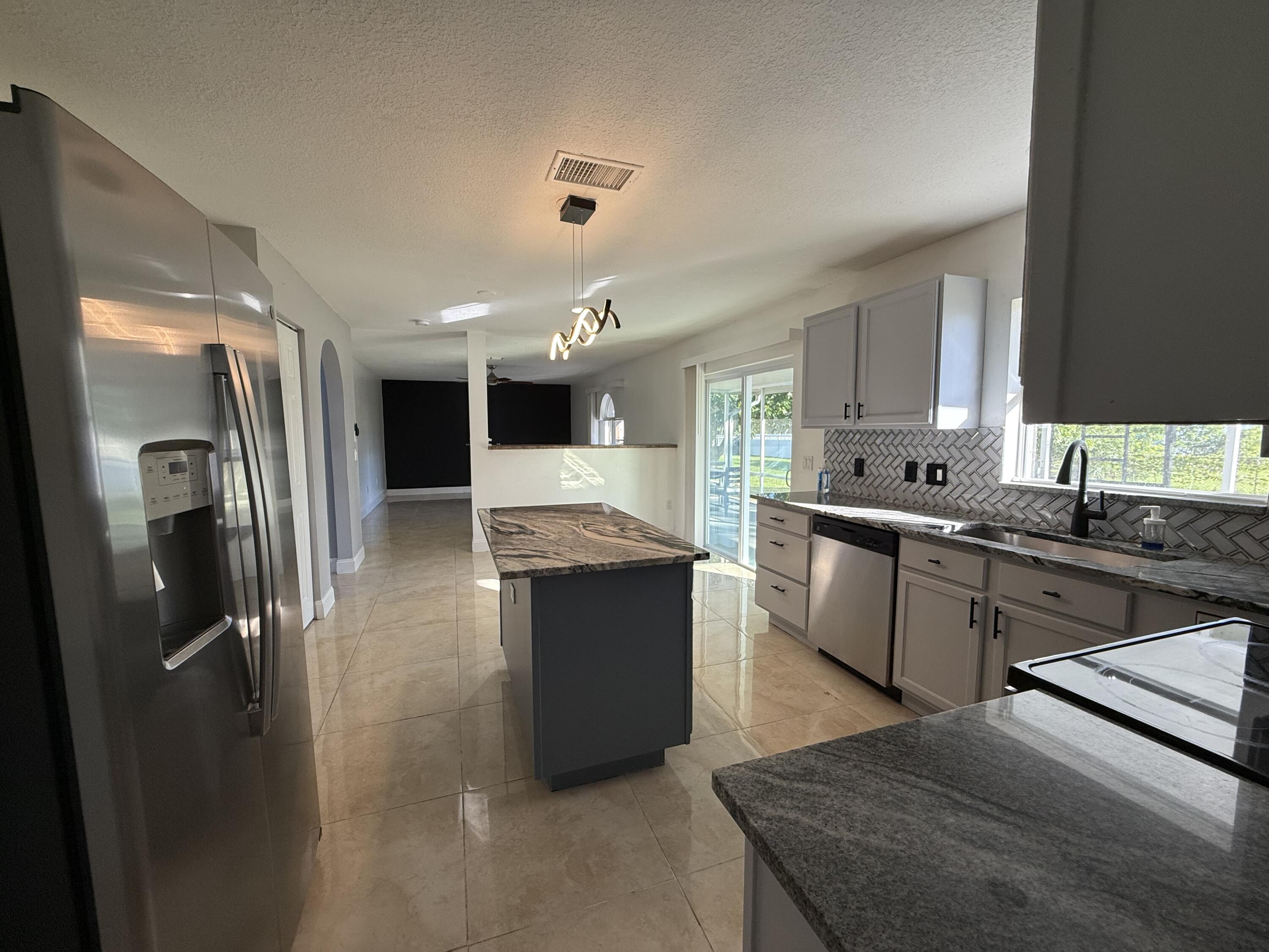 1925 Southwest Libra Lane Port St. Lucie, FL 34984 - Photo 15 of 49 a large kitchen with stainless steel appliances kitchen island granite countertop a refrigerator and a sink