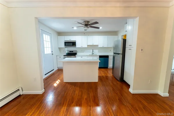 a kitchen with kitchen island a sink a stove a refrigerator and white cabinets with wooden floor