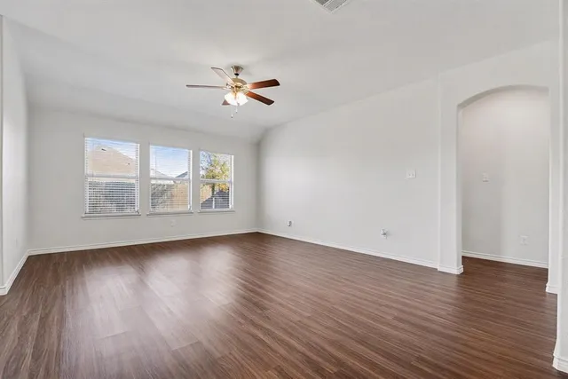 an empty room with wooden floor chandelier fan and windows