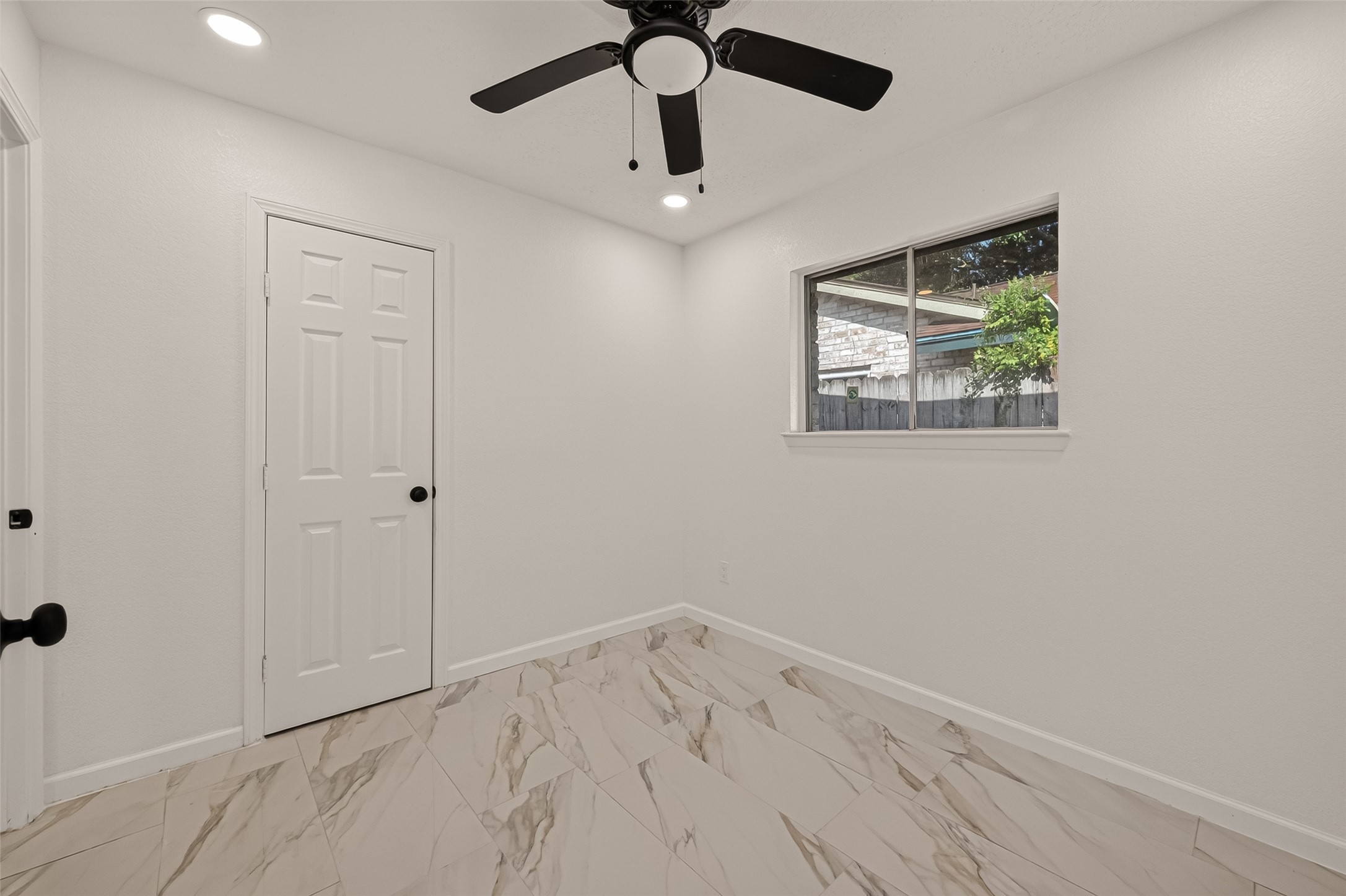 16619 Tibet Road Friendswood, TX 77546 - Photo 22 of 29 This room features sleek marble-patterned flooring, a ceiling fan, and a window offering natural light. The white walls and ceiling create a fresh, modern look, while the interior door complements the clean design.