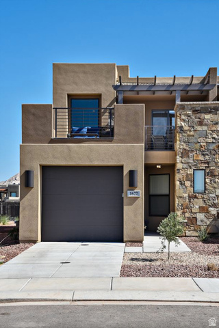 1622 Canyon Tree Drive St. George, UT 84770 - Photo 1 of 34 Stucco exterior with stone accent facade, featuring a dark tone garage door, an upper balcony with metal railing, and a second-story patio with pergola