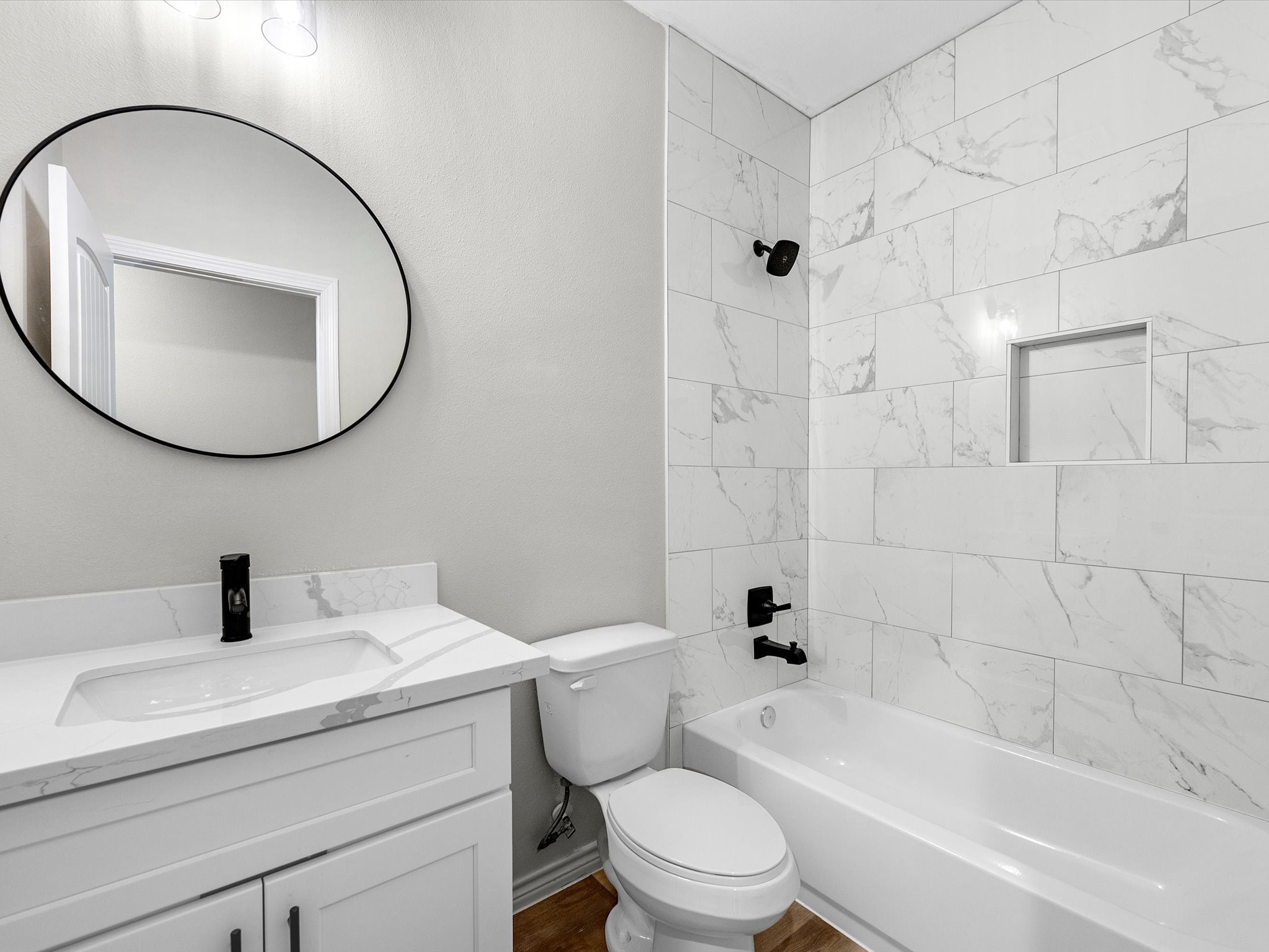 1319 West Bell Street Houston, TX 77019 - Photo 33 of 50 This modern bathroom features a sleek design with a white vanity and black fixtures. It includes a large circular mirror, a bathtub with marble-look tiles, and a built-in shower niche.