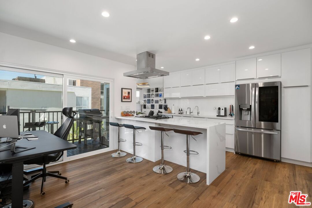 949 North Kings Road, Unit 302 West Hollywood, CA 90069 - Photo 6 of 16 a kitchen with stainless steel appliances kitchen island granite countertop a table chairs refrigerator and microwave
