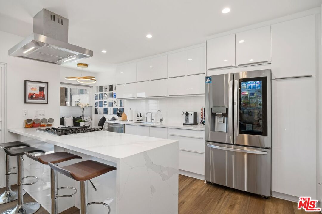 949 North Kings Road, Unit 302 West Hollywood, CA 90069 - Photo 7 of 16 a kitchen with granite countertop a refrigerator a stove a sink and white cabinets with wooden floor