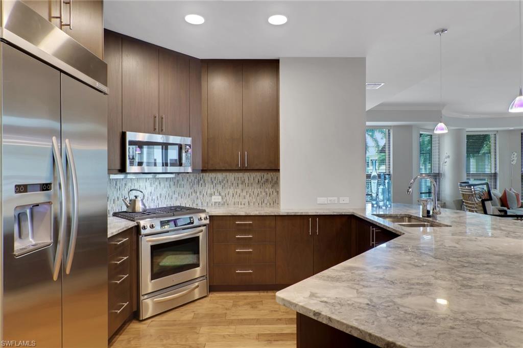 9123 Strada Place, Unit 7216 Naples, FL 34108 - Photo 2 of 28 Kitchen featuring stainless steel appliances, light stone countertops, light wood-style floors, hanging light fixtures, and a peninsula