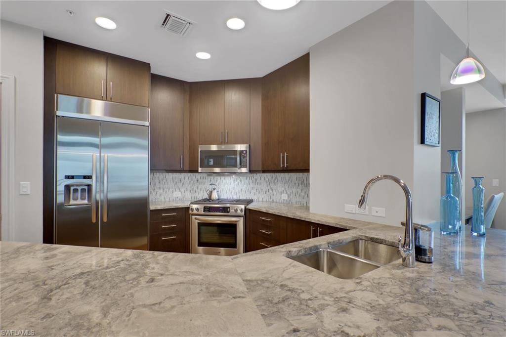 9123 Strada Place, Unit 7216 Naples, FL 34108 - Photo 4 of 28 Kitchen featuring stainless steel appliances, light stone countertops, tasteful backsplash, dark wood finish cabinets, and pendant lighting