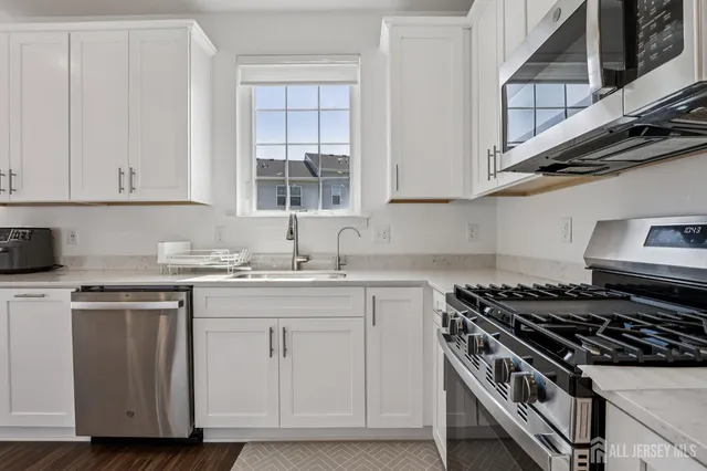 a kitchen with stainless steel appliances a refrigerator a sink dishwasher a stove and white cabinets with wooden floor