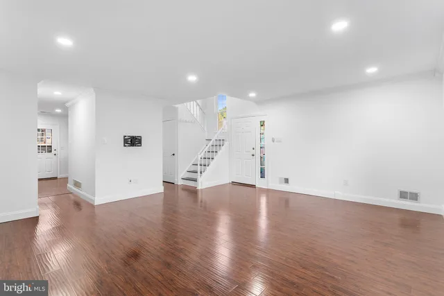 a view of an empty room with wooden floor and a kitchen
