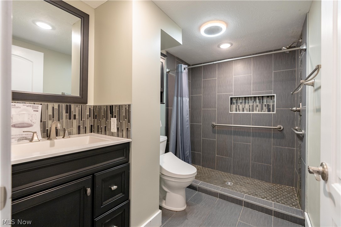 6116 Melody Road Northeast Canton, OH 44721 - Photo 26 of 33 Bathroom with vanity, a stall shower, backsplash, a textured ceiling, and dark tile patterned floors