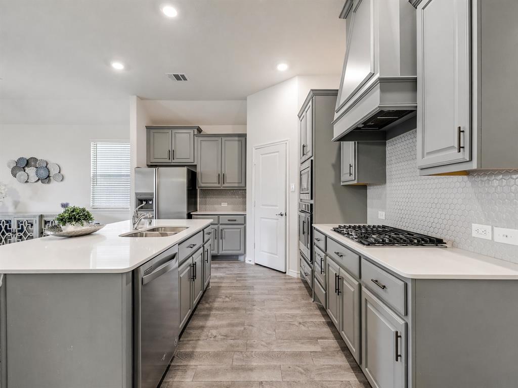 3024 Meredith Lane Forney, TX 75126 - Photo 20 of 29 Spacious kitchen featuring an expansive island with a double basin sink, stainless steel appliances, shaker-style cabinetry, and wood-finish flooring