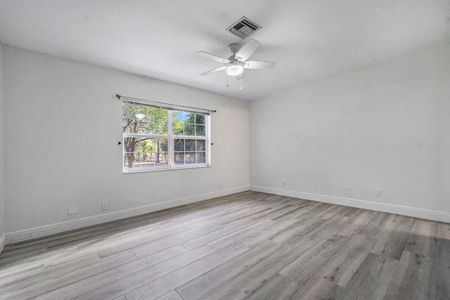 an empty room with wooden floor chandelier fan and windows