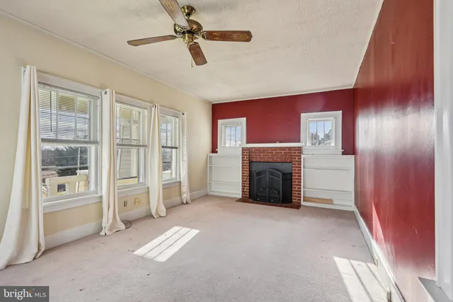 an empty room with windows fireplace and a ceiling fan