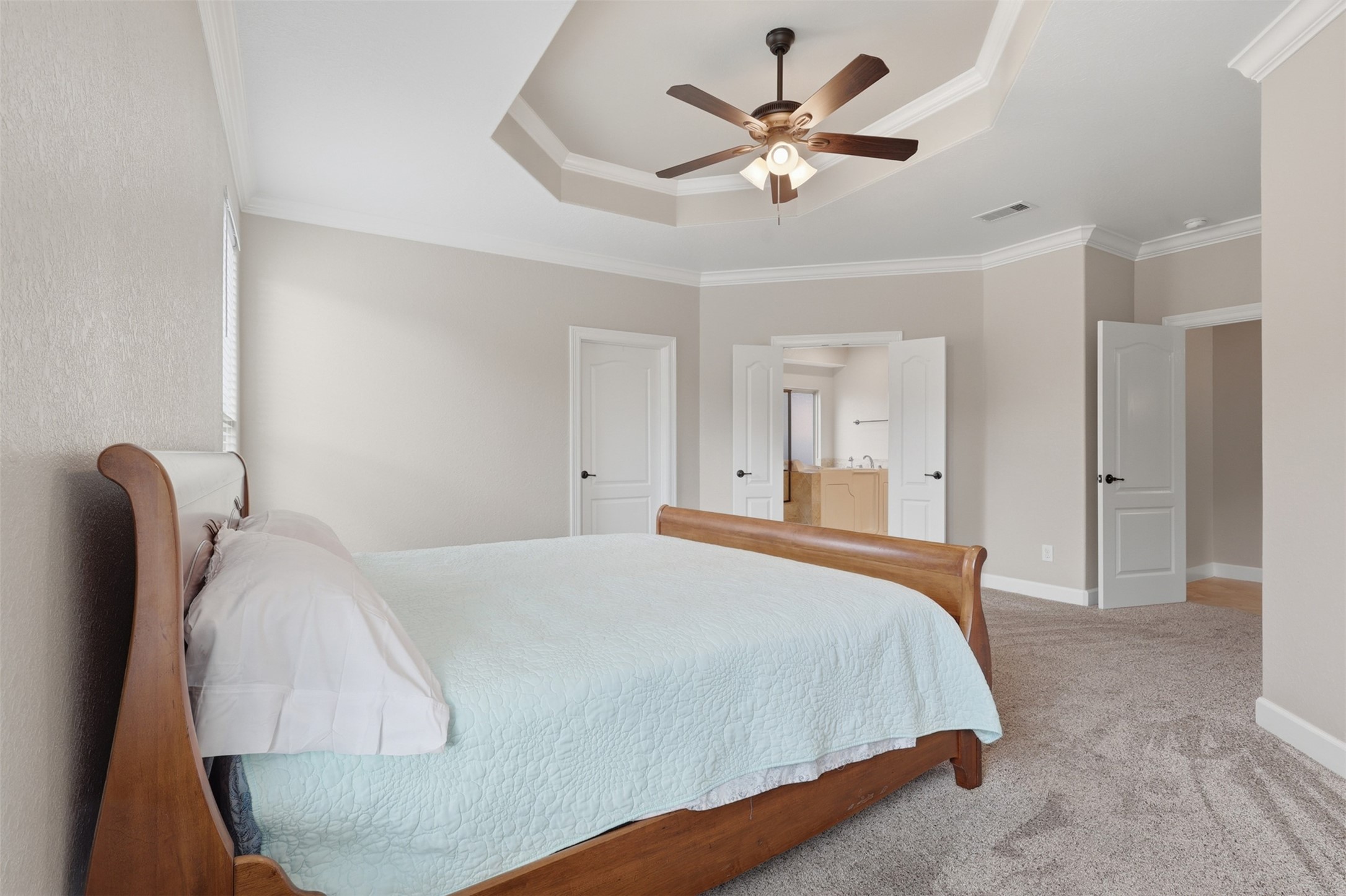 721 Rufina Street League City, TX 77573 - Photo 14 of 33 Another view highlights the impressive scale of the primary retreat, complete with a decorative tray ceiling, ceiling fan, and direct access to the luxurious ensuite bath. Soft neutral tones and fresh finishes provide a timeless backdrop ready for any design style.