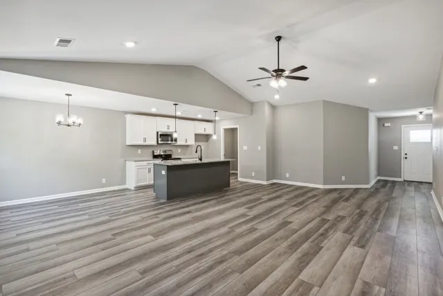 an empty room with wooden floor a ceiling fan and kitchen view