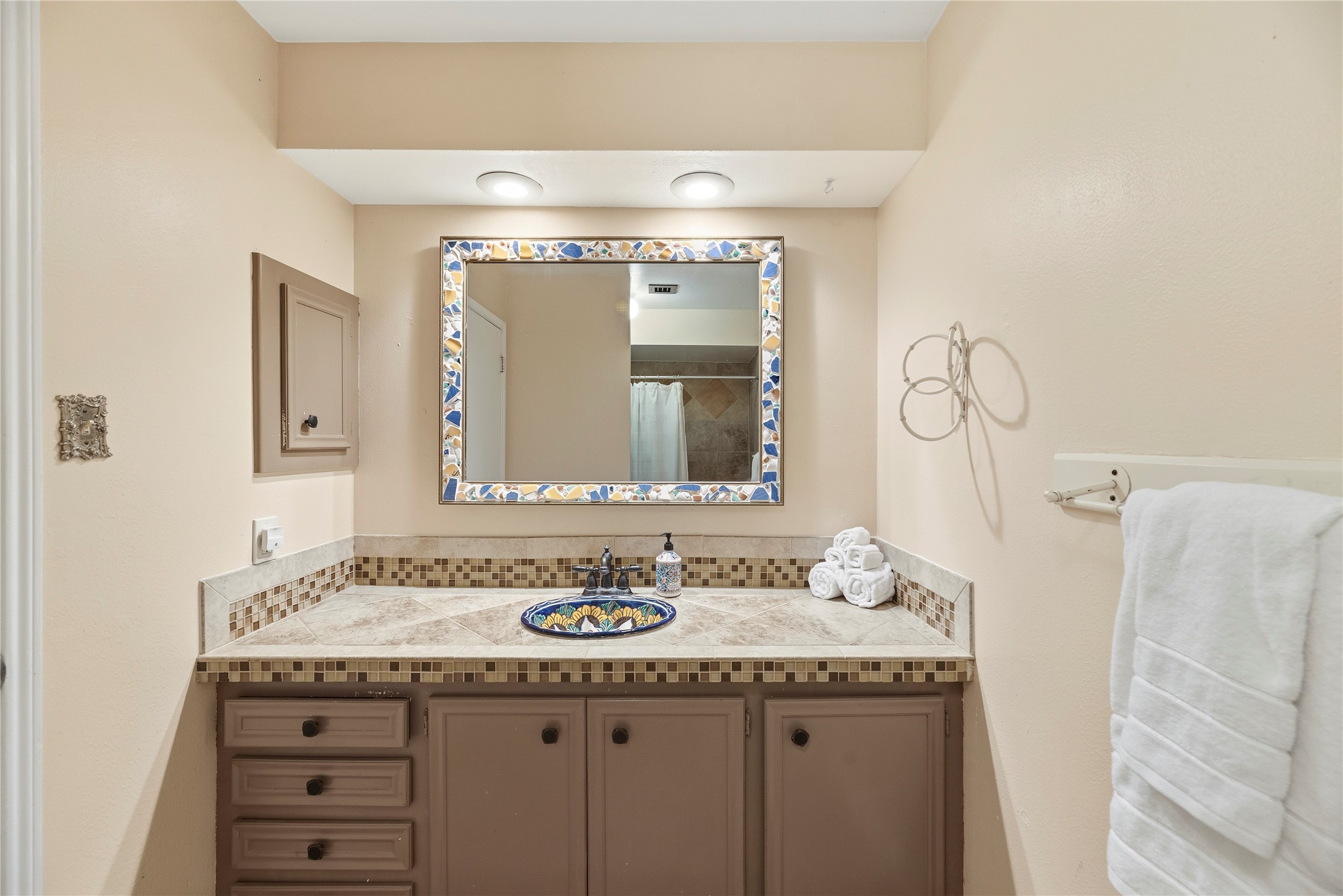 14203 Wickersham Lane Houston, TX 77077 - Photo 16 of 25 Full bathroom highlighting a custom-tiled vanity countertop with a hand-painted ceramic vessel sink, a multi-colored mosaic-framed mirror, and a peek at the tile-surfaced shower area reflected in the glass.