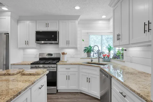 a kitchen with stainless steel appliances granite countertop a refrigerator oven a sink dishwasher and white cabinets with wooden floor