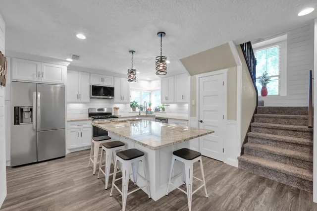 a kitchen with stainless steel appliances granite countertop a dining table chairs stove a refrigerator and cabinets