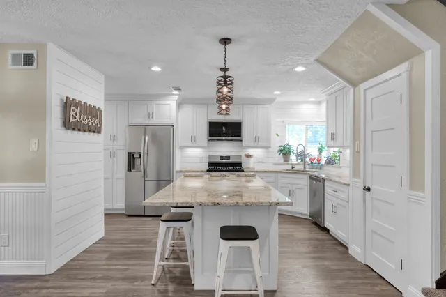 a kitchen with stainless steel appliances a dining table chairs refrigerator and sink