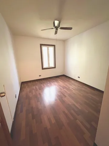 an empty room with wooden floor chandelier fan and windows