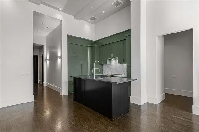 an empty room with wooden floor and way to kitchen