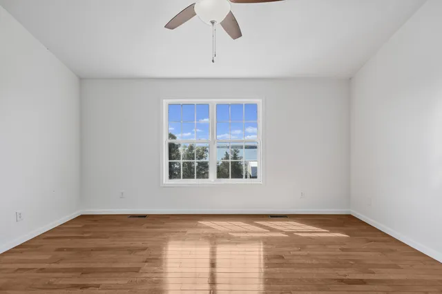a view of empty room with wooden floor and ceiling fan