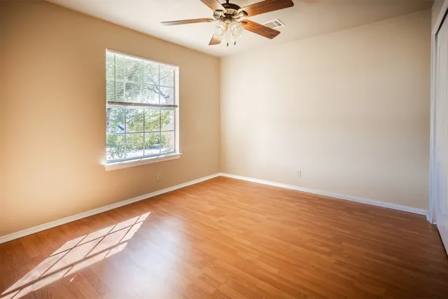an empty room with wooden floor chandelier fan and windows