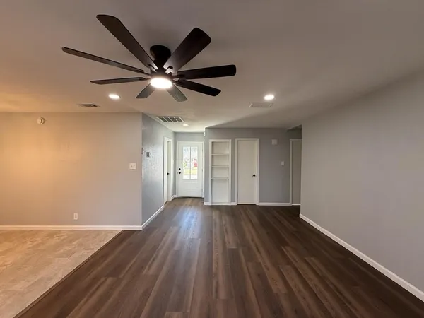 a view of an empty room with wooden floor and a ceiling fan