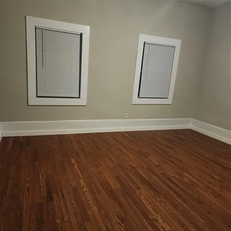 a view of an empty room with wooden floor and windows