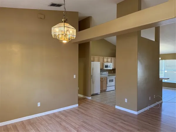 an empty room with wooden floor a kitchen view and windows