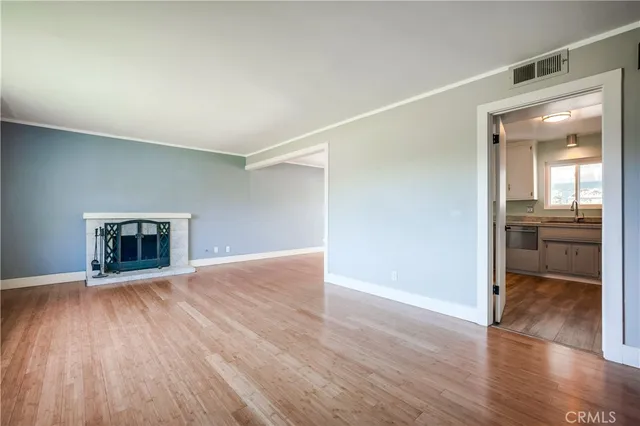 an empty room with wooden floor and a kitchen