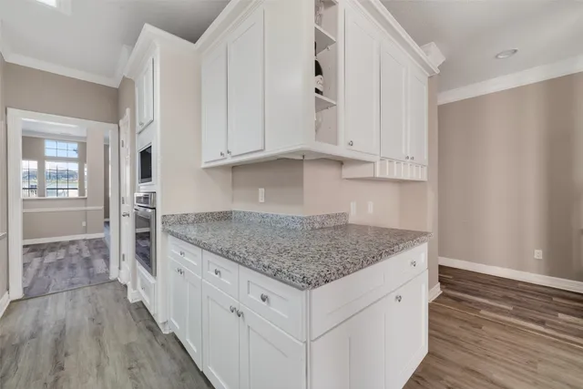 a kitchen with stainless steel appliances granite countertop a stove top oven a refrigerator and white cabinets with wooden floor