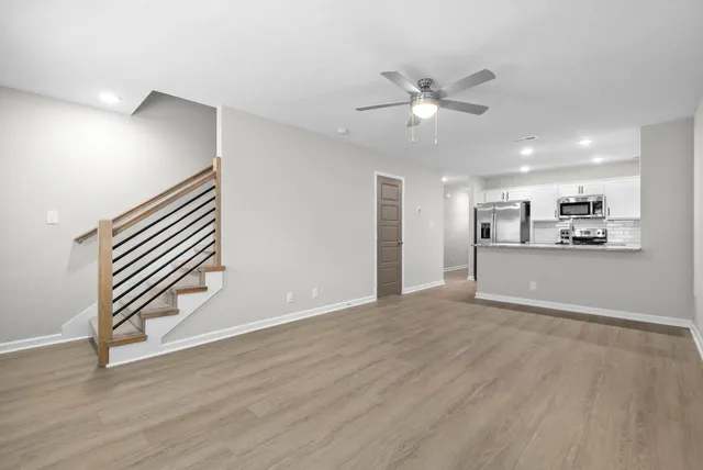 a view of an empty room with wooden floor and a ceiling fan