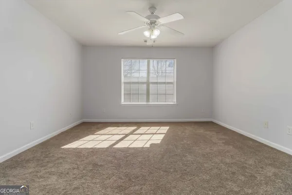 an empty room with chandelier fan and windows