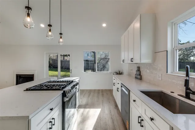 a kitchen with stainless steel appliances kitchen island a white stove a sink dishwasher and white cabinets with wooden floor