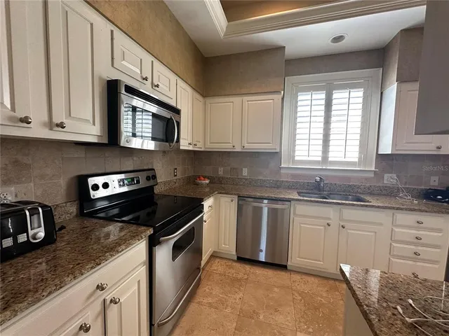 a kitchen with granite countertop white cabinets stainless steel appliances a sink and a window