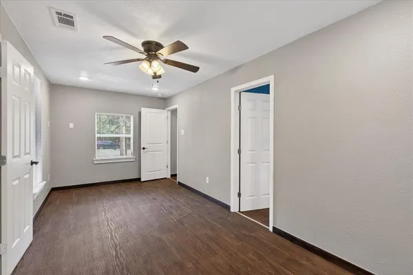 an empty room with wooden floor chandelier fan and windows