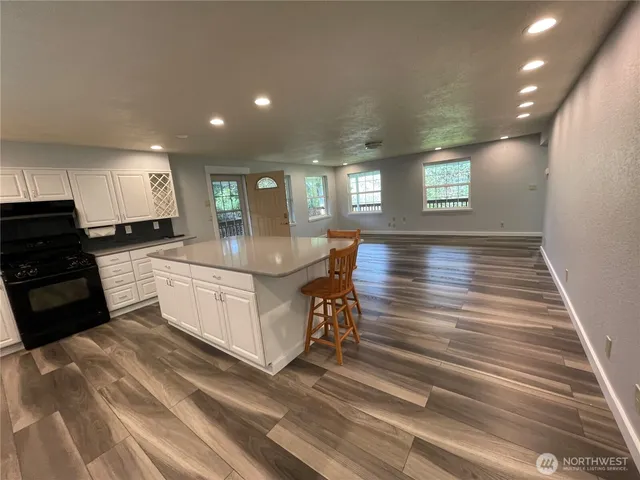 a kitchen with granite countertop a stove top oven a sink dishwasher and white cabinets with wooden floor