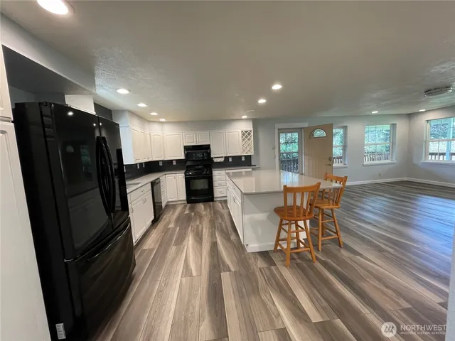 an open kitchen with kitchen island wooden floor and stainless steel appliances