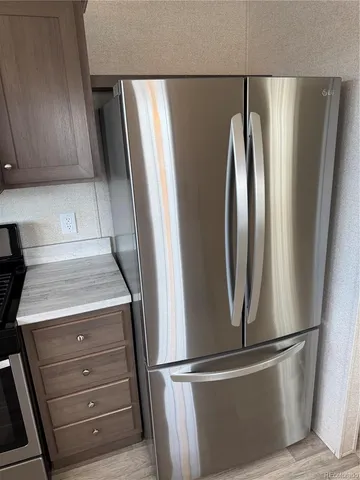 a view of a refrigerator in kitchen and an empty room with wooden floor