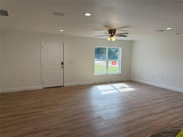 an empty room with wooden floor ceiling fan and windows