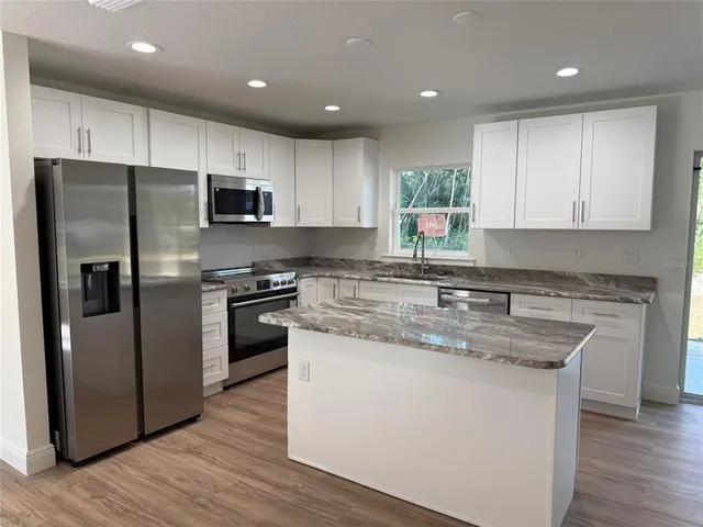 a kitchen with stainless steel appliances granite countertop a refrigerator a sink dishwasher a stove and oven with wooden floor