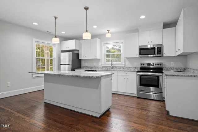 a view of an empty room with wooden floor and a kitchen