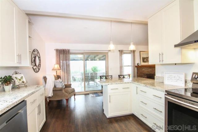 a kitchen with a stove a sink and white cabinets with wooden floor next to windows