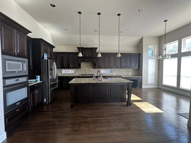 a kitchen with stainless steel appliances granite countertop a sink a stove and a wooden floors