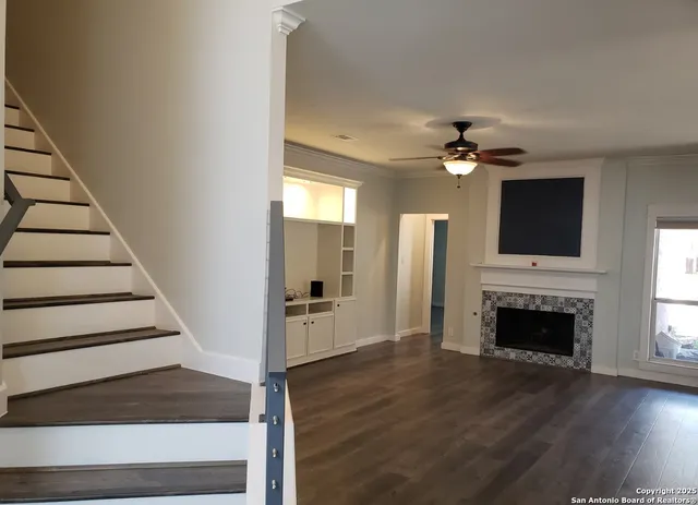 a view of a livingroom with a fireplace a ceiling fan and wooden floor