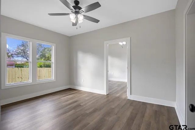 an empty room with wooden floor chandelier fan and windows