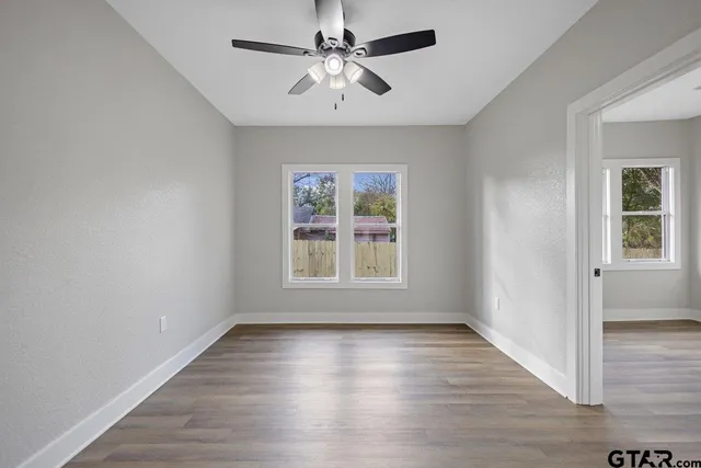 an empty room with wooden floor chandelier fan and windows