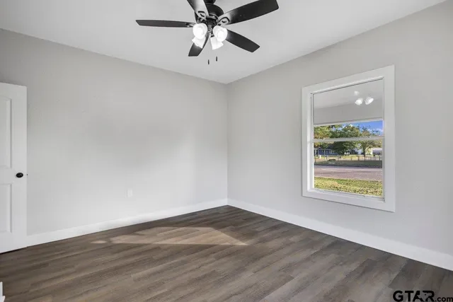 an empty room with wooden floor chandelier fan and windows
